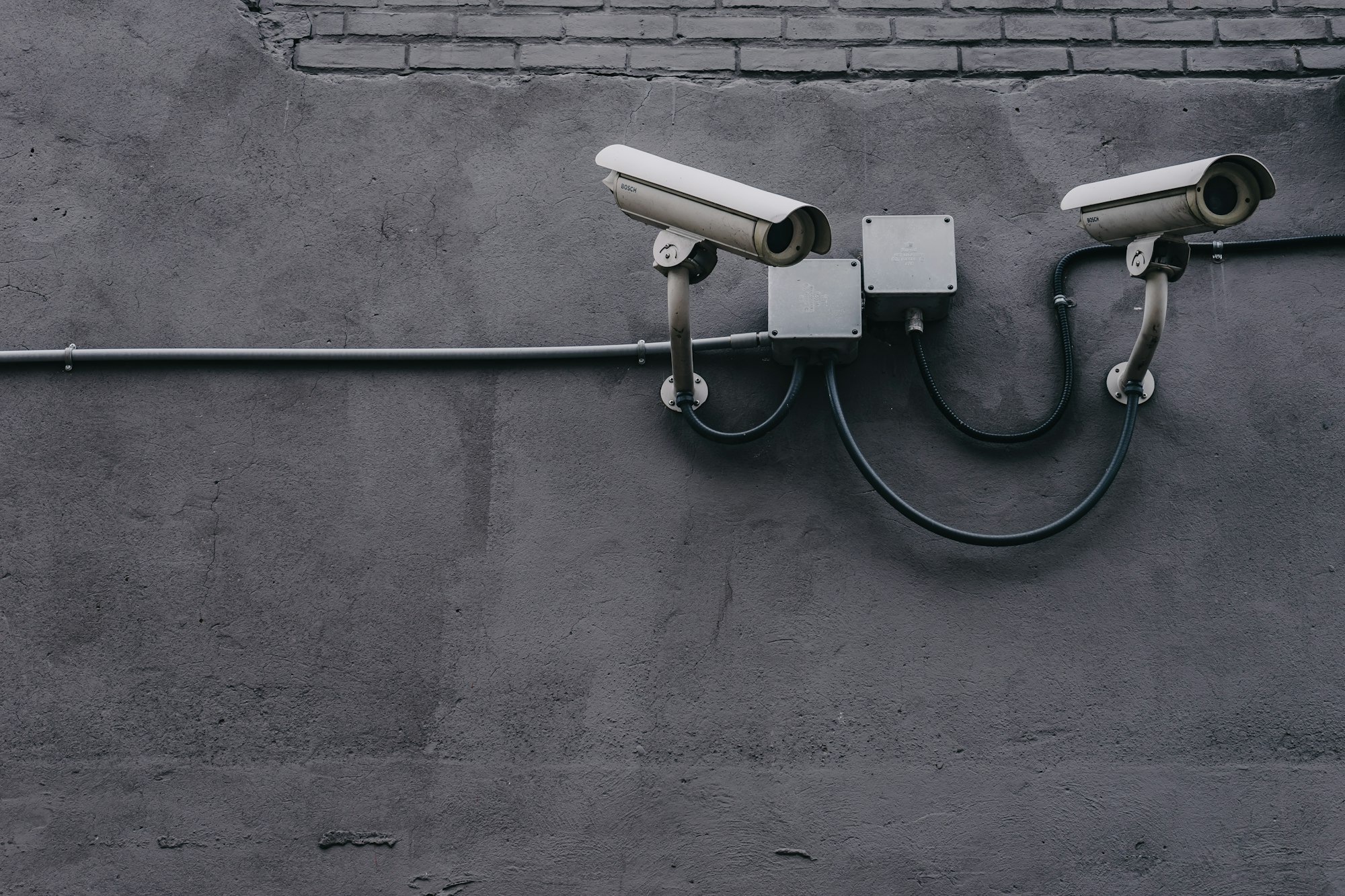 Ageing CCTV cameras and exposed conduit on a concrete wall, the kind of system a CCTV upgrade replaces