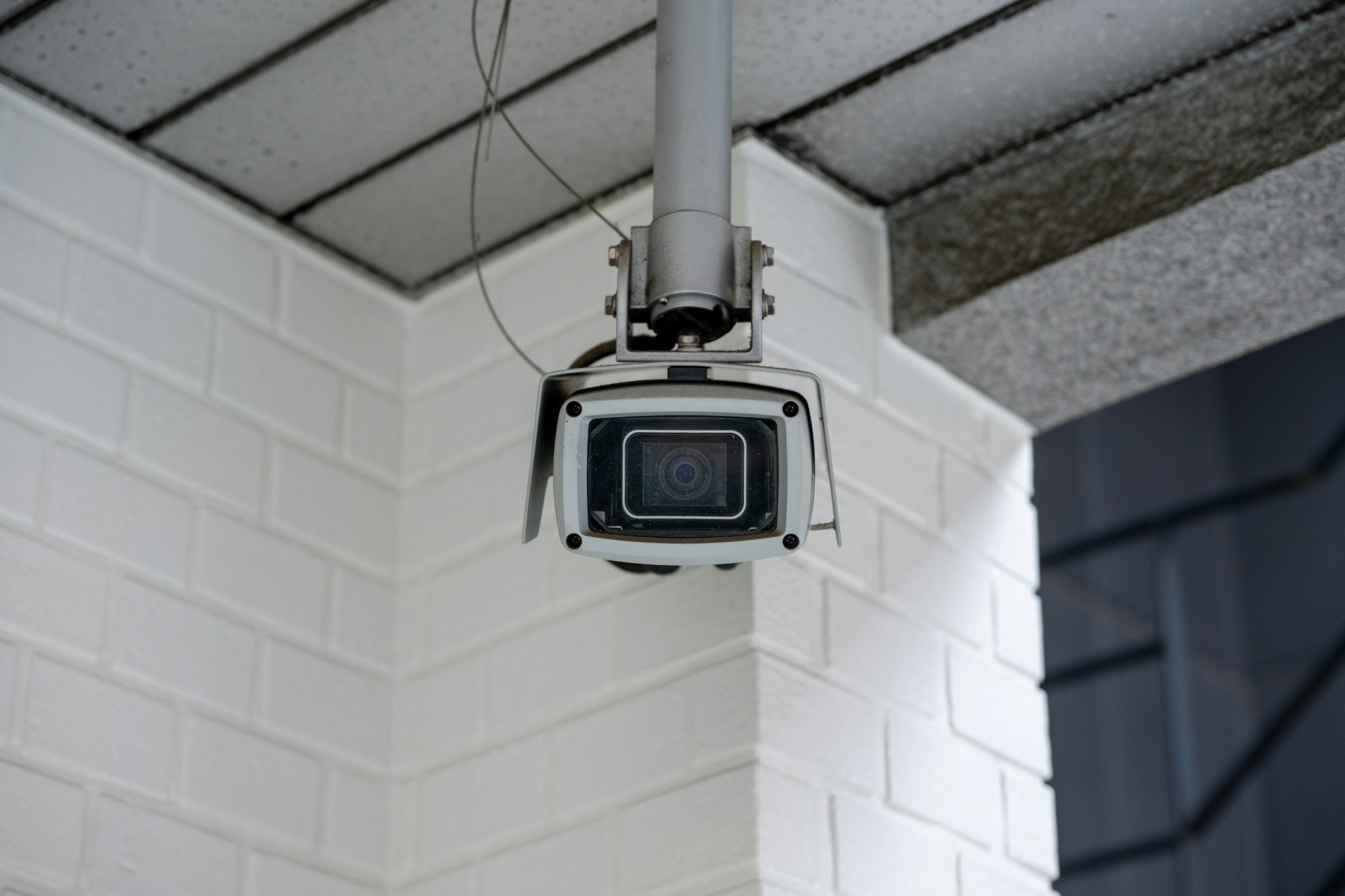 Box camera in a weatherproof housing on a ceiling mount, typical of an analogue system awaiting a CCTV upgrade